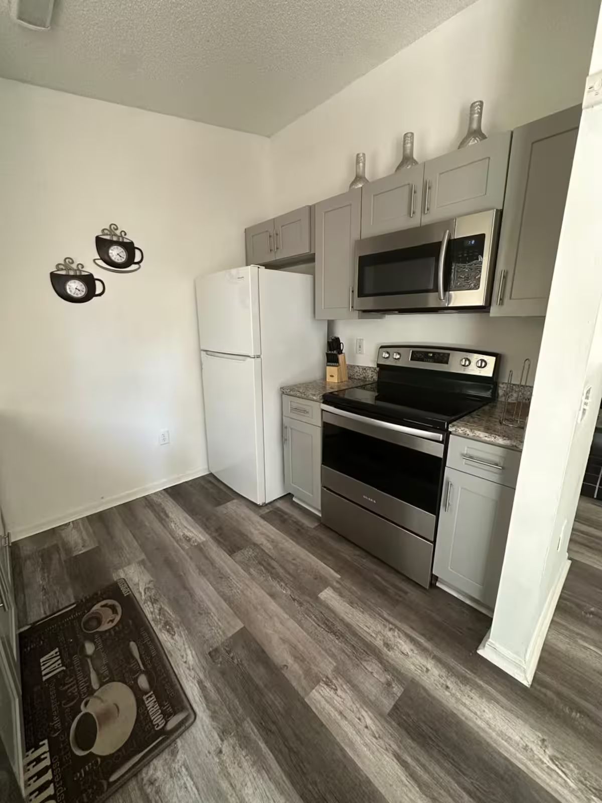 A compact kitchen with white cabinets, a stainless steel refrigerator, a microwave, and an oven.