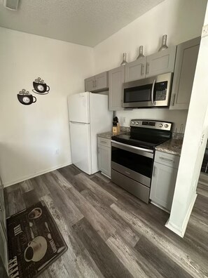 Eine kleine Küche mit weißen Schränken, einem Edelstahlkühlschrank, einer Mikrowelle und einem Backofen.