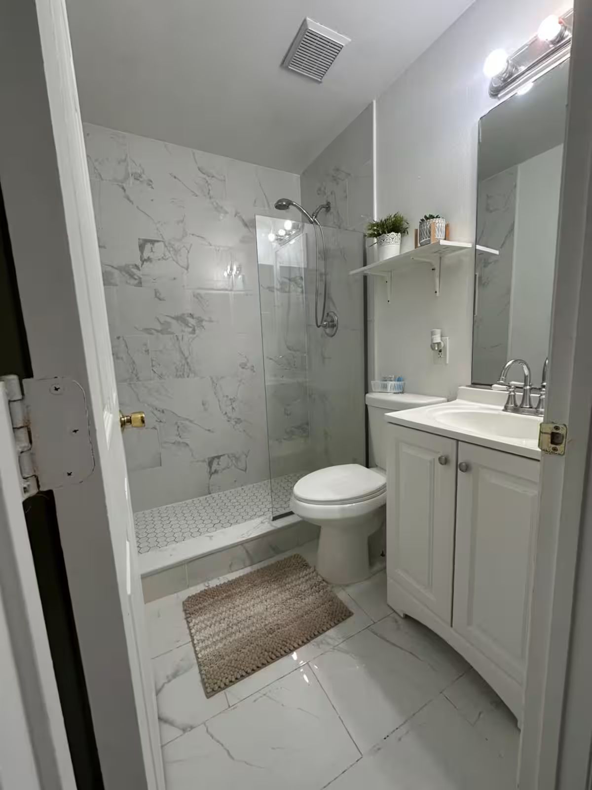 A bathroom with a shower, toilet, sink, and a mirror.