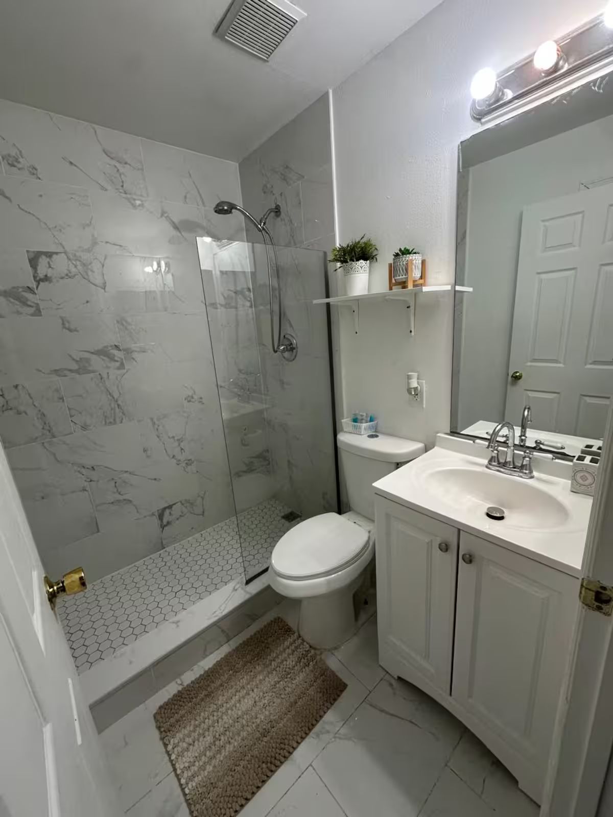 Un baño con ducha, inodoro, lavamanos y un espejo grande.