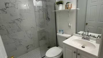 Un baño con ducha, inodoro, lavamanos y un espejo grande.