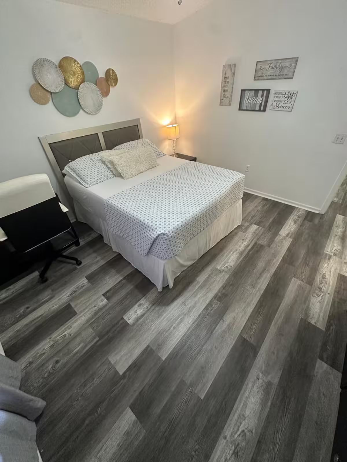 Ein Schlafzimmer mit einem Bett, einem Schreibtisch und einem Sessel. Es gibt Wanddekorationen und eine Lampe.