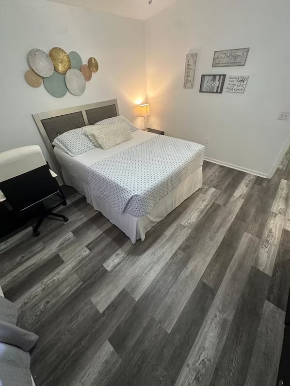 Un dormitorio con cama, escritorio y silla. Decoración en las paredes y una lámpara.
