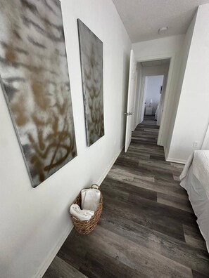 A hallway with a wooden floor, a white wall, and a wicker basket with a pillow.