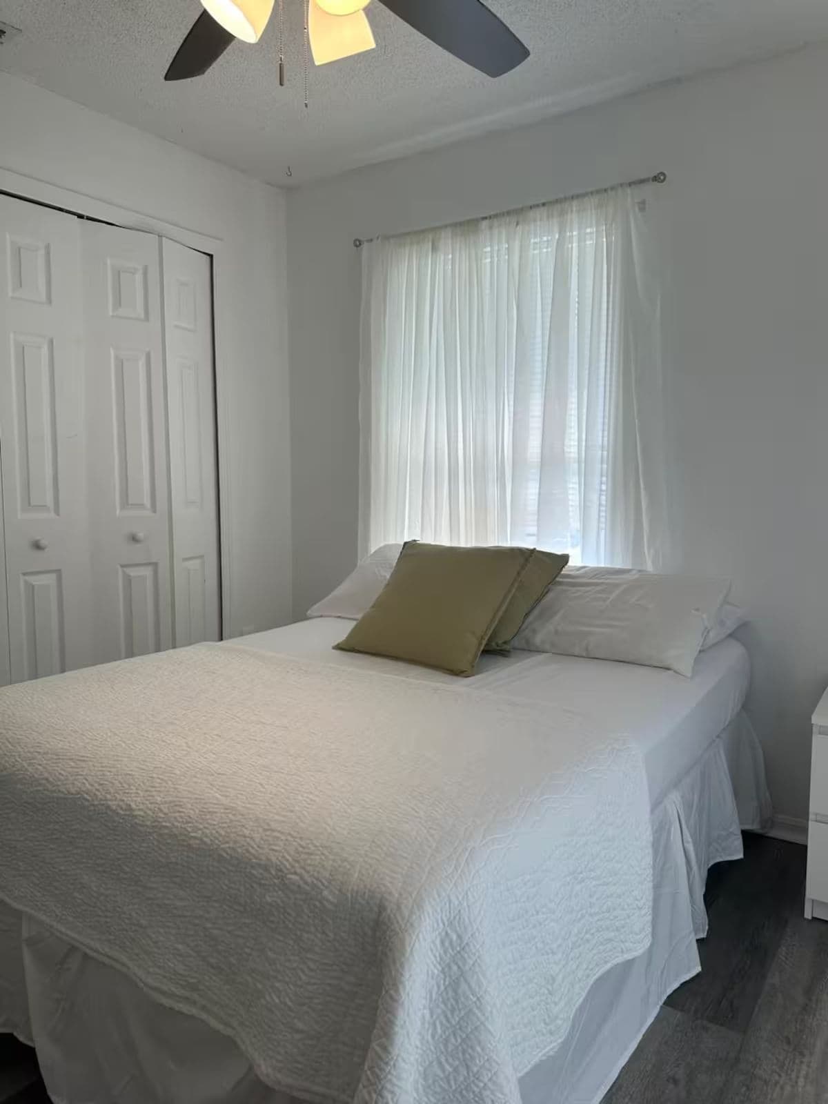 Ein Schlafzimmer mit einem Bett, weißen Vorhängen, einem Deckenventilator und einer weißen Tür.