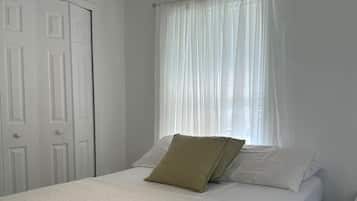Ein Schlafzimmer mit einem Bett, weißen Vorhängen, einem Deckenventilator und einer weißen Tür.