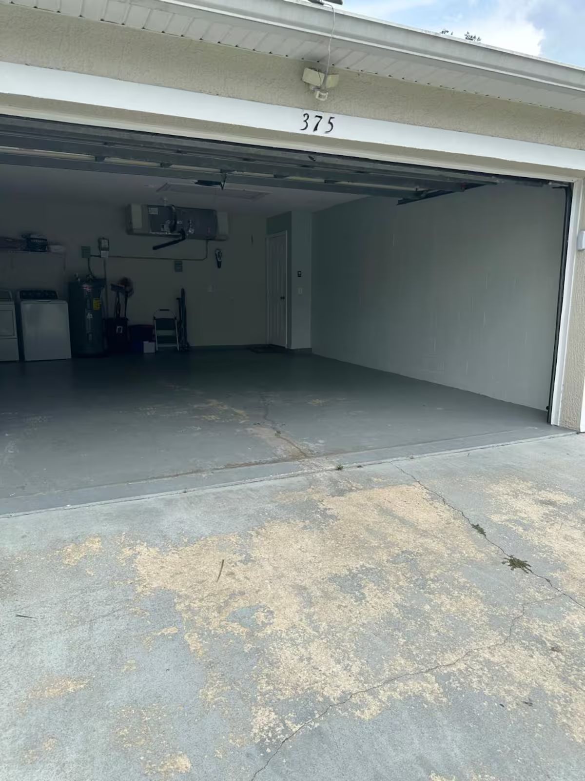 Een garage met een betonnen vloer, een boiler en een deur met het nummer 375 erop.