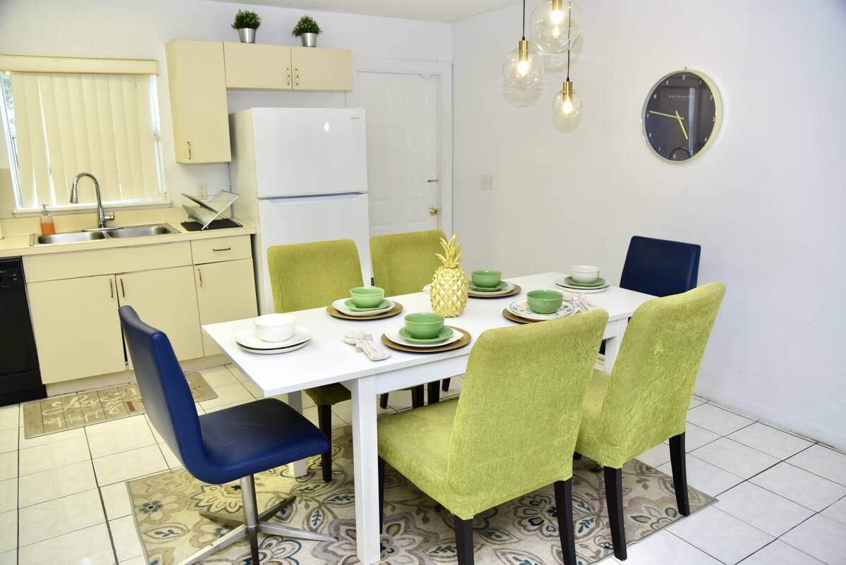 Una cocina funcional con un refrigerador blanco, un lavamanos y una zona de comedor con una mesa blanca y sillas verdes.