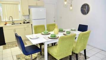 Una cocina funcional con un refrigerador blanco, un lavamanos y una zona de comedor con una mesa blanca y sillas verdes.