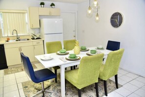 A compact kitchen with a white refrigerator, a sink, and a dining area with a white table and green chairs.