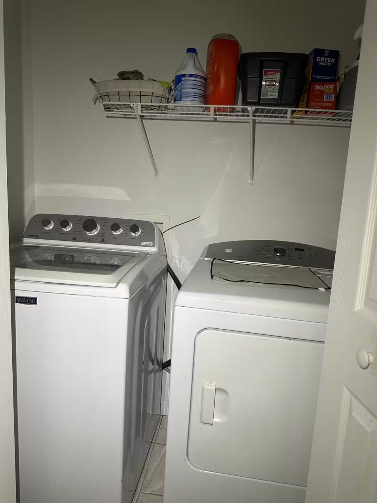 A laundry room with two washing machines and a shelf above containing a water bottle, a red container, and a box labeled 'DRYER SHEETS'.
