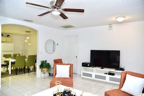 A living room with a ceiling fan, a flat-screen TV, a dining area with chairs, and a sofa.