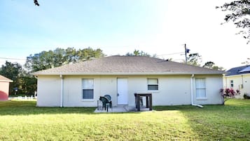 A single-story house with a front door, a small porch with a table and chairs, and a well-maintained lawn.