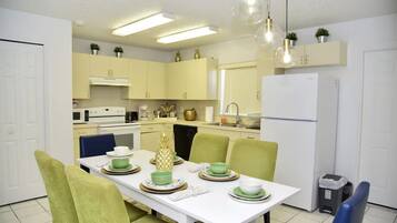 A modern kitchen with a white table set for dining, green chairs, and a refrigerator.