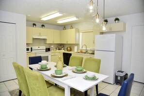 Een moderne keuken met een witte eettafel, groene stoelen en een koelkast.