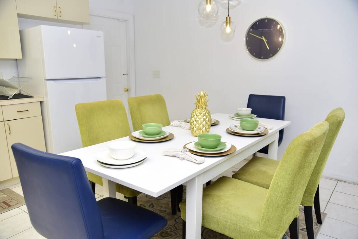 A dining area with a white table set for four, green chairs, and a pineapple centerpiece.