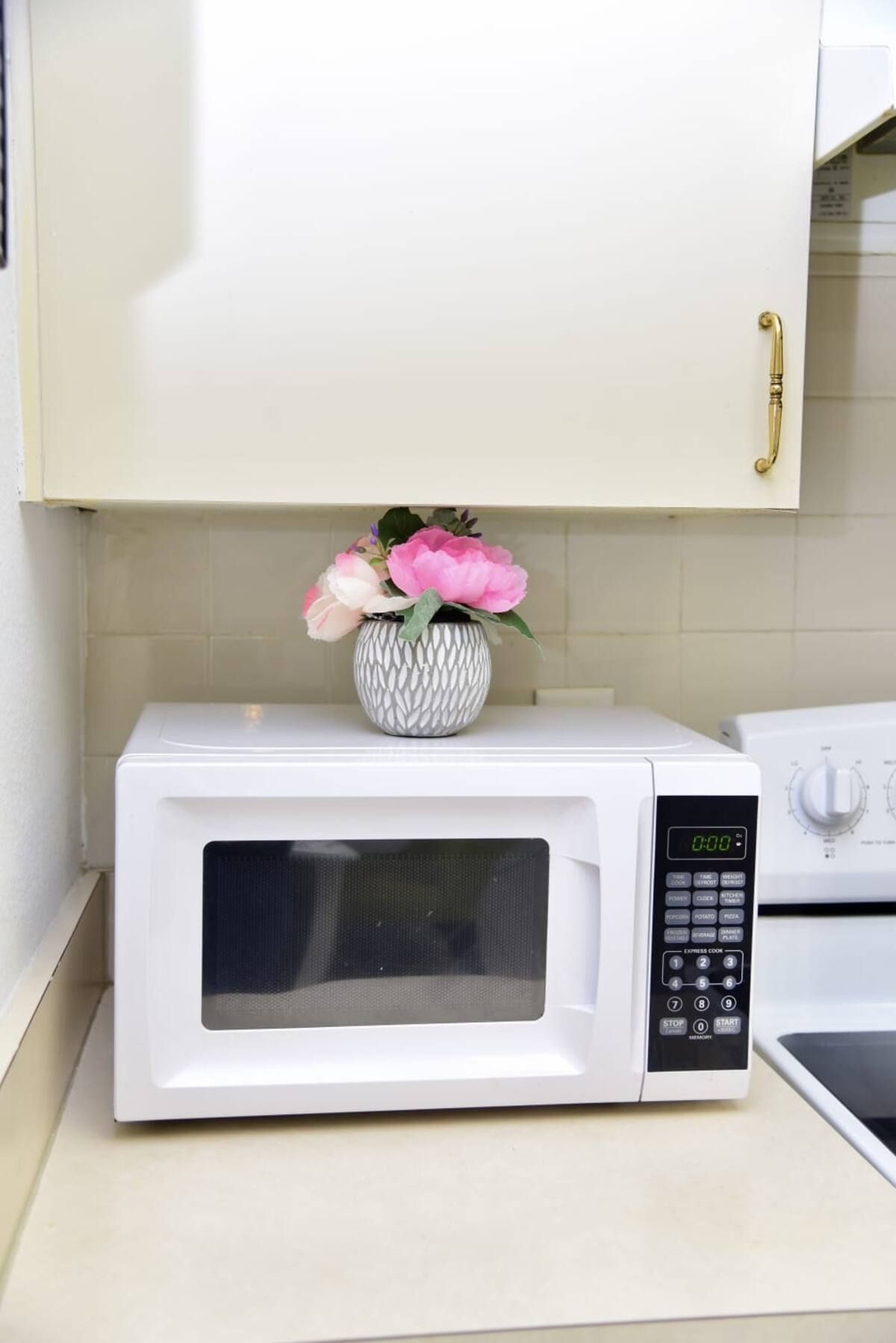 A white microwave oven on a kitchen counter with a decorative vase containing pink flowers.