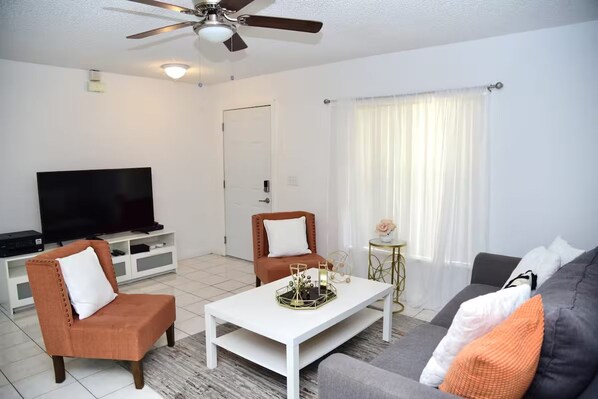 A living room with a flat-screen TV, two armchairs, a coffee table, and a sofa.