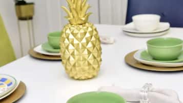 A dining table with a pineapple centerpiece, green bowls, and gold-rimmed plates.