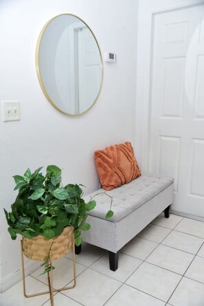 A hallway with a grey bench, a round mirror, a potted plant, and a door.