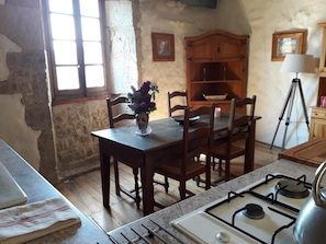 A rustic kitchen with a wooden table, chairs, a gas stove, and a window with a view. - Gite 'Cap Del Mas' with Private Terrace and Wi-Fi (Ambeyrac)