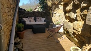 Ein Sitzbereich im Freien mit Steinwänden, einer Couch und Kissen, einem Klappstuhl und Topfpflanzen.