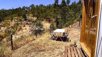 A wooden cabin with a table and chairs outside, surrounded by dry grass and sparse vegetation.