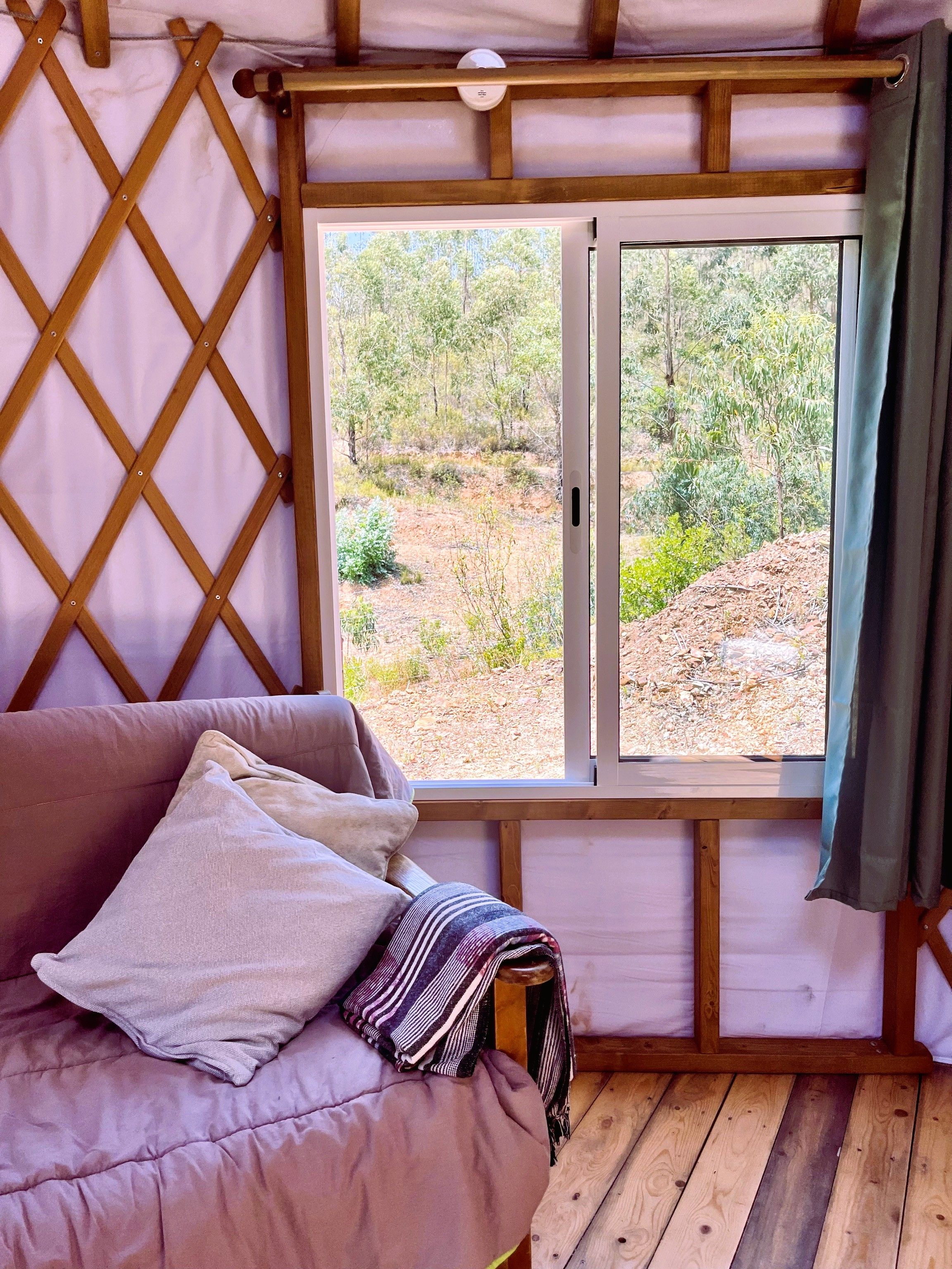 Ein Zimmer mit einem hölzernen Bett, einem Fenster mit Blick auf Bäume und einer Holzwand mit Gitterwerk.
