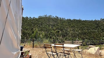 Un camping con una mesa y sillas, rodeado de hierba seca y una colina boscosa.