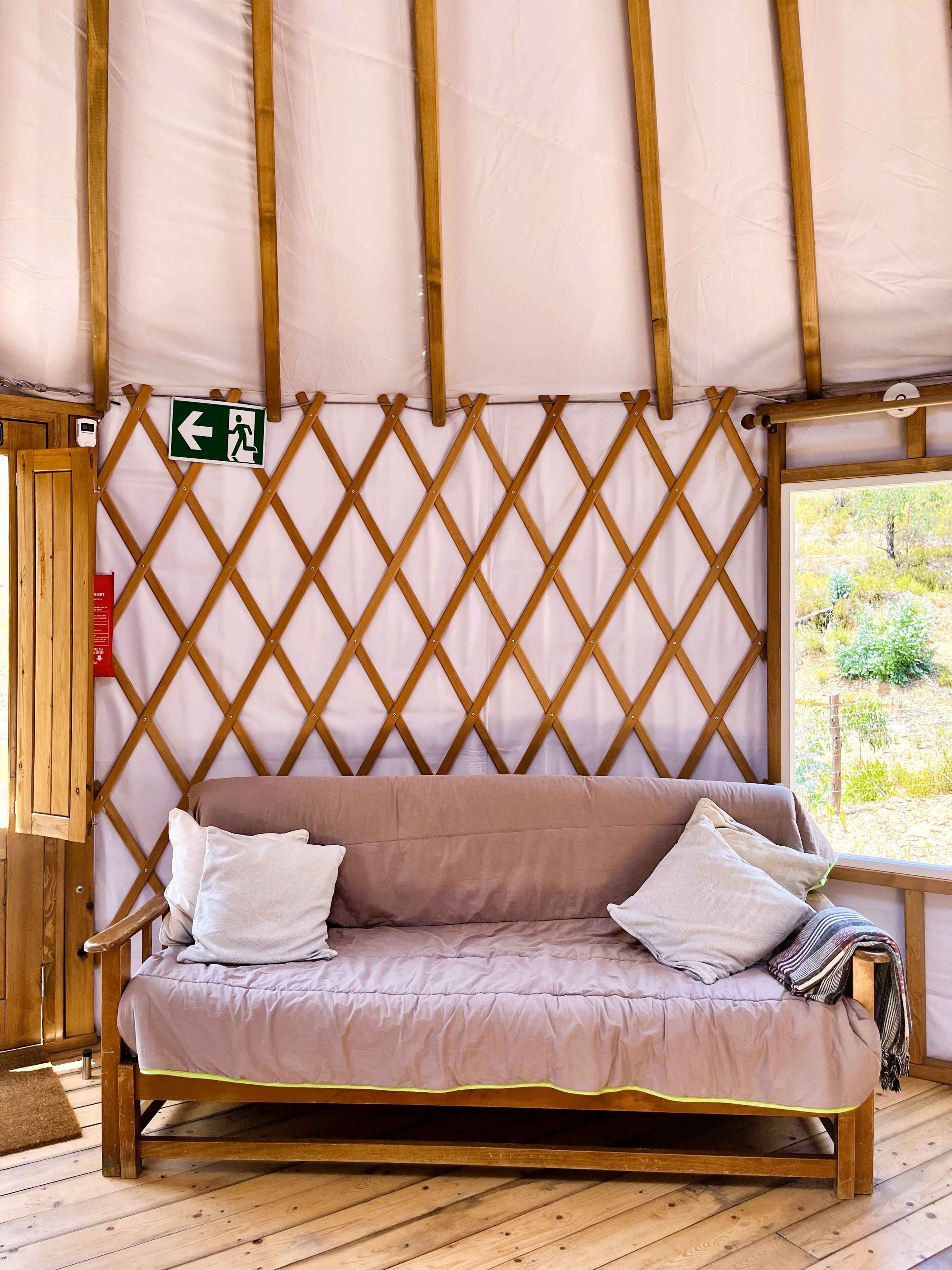 A wooden sofa with cushions, a lattice wall, and a view of greenery outside.