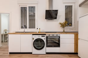 A compact kitchen with a washing machine, oven, and a flat-screen TV mounted above the counter. - Newly renovated in the heart of Madrid (Madrid)