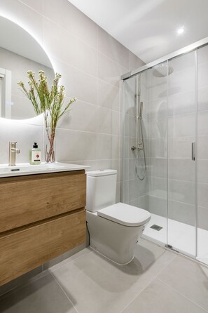 A modern bathroom with a toilet, a shower enclosure, a vanity with a mirror, and a plant. - Newly renovated in the heart of Madrid (Madrid)