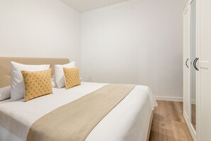 A neatly made bed with a beige headboard, white bedding, and two patterned pillows. - Newly renovated in the heart of Madrid (Madrid)