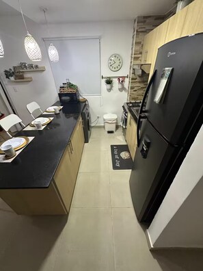 A compact kitchen with a black refrigerator, a sink, and a dining area with chairs and plates. - Punta Cana Paraiso Tropical Playas de Mar Caribeño (Punta Cana)
