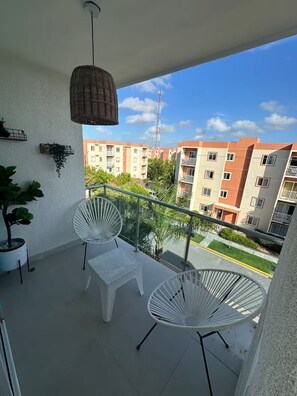 Ein Balkon mit zwei weißen Stühlen, einer hängenden Ampel und einem Blumentopf.