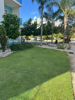 A well-maintained grassy area with trees and a building in the background. - Punta Cana Paraiso Tropical Playas de Mar Caribeño (Punta Cana)
