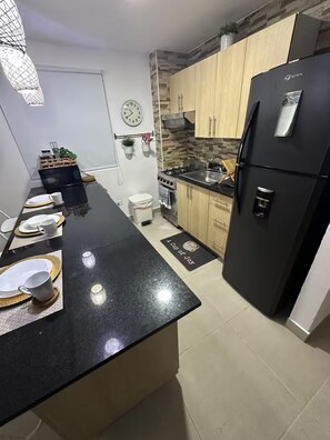 A modern kitchen with a black countertop, a refrigerator, and wooden cabinets. - Punta Cana Paraiso Tropical Playas de Mar Caribeño (Punta Cana)