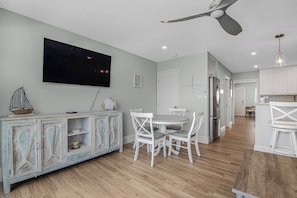 A dining area with a white table and chairs, a ceiling fan, and a television mounted on the wall. - Oceanfront Key Colony Beach Condo with Private Balcony, Sandy Shoreline & Sweeping Atlantic Views (Key Colony Beach)