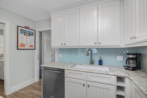 A kitchen with white cabinets, a stainless steel dishwasher, a sink with a modern faucet, and a coffee maker. - Oceanfront Key Colony Beach Condo with Private Balcony, Sandy Shoreline & Sweeping Atlantic Views (Key Colony Beach)