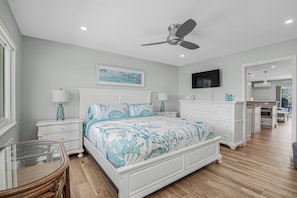 A bedroom with a bed, bedside tables, a ceiling fan, a TV, and a bathroom visible in the background. - Oceanfront Key Colony Beach Condo with Private Balcony, Sandy Shoreline & Sweeping Atlantic Views (Key Colony Beach)
