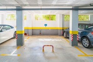 A parking garage with two cars parked, concrete pillars, yellow and white painted lines, and a blue parking sign. - Cubo's Opalo de Riviera Apartment / communal pool / communal gym / air conditioning / terrace (Mijas Costa)