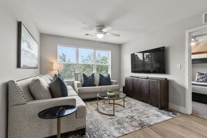Ein modernes Wohnzimmer mit einer Couch, einem Couchtisch, einem Fernseher und einem Deckenventilator.