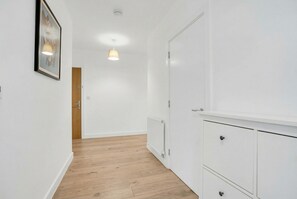 A corridor with white walls, a wooden floor, a radiator, and a door. - 2-Bed 2-Bath London Apartment, Fast Transport Links - Business & Long Stays (LONDON)