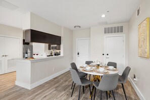 A modern kitchen with a central island, a dining area with a round table and four chairs, and a white door with a vent above it. - 2-bedroom apartment in adorable Dallas with cool AC and gym access (Dallas)