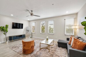 A modern living room with a flat-screen TV, a ceiling fan, and a large window with blinds. - 2-bedroom apartment in adorable Dallas with cool AC and gym access (Dallas)