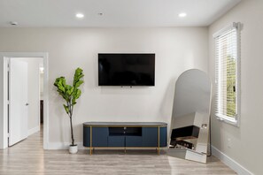 A modern living room with a flat-screen TV mounted on the wall, a blue console table with gold legs, a potted plant, and a large mirror reflecting the room. - 2-bedroom apartment in adorable Dallas with cool AC and gym access (Dallas)
