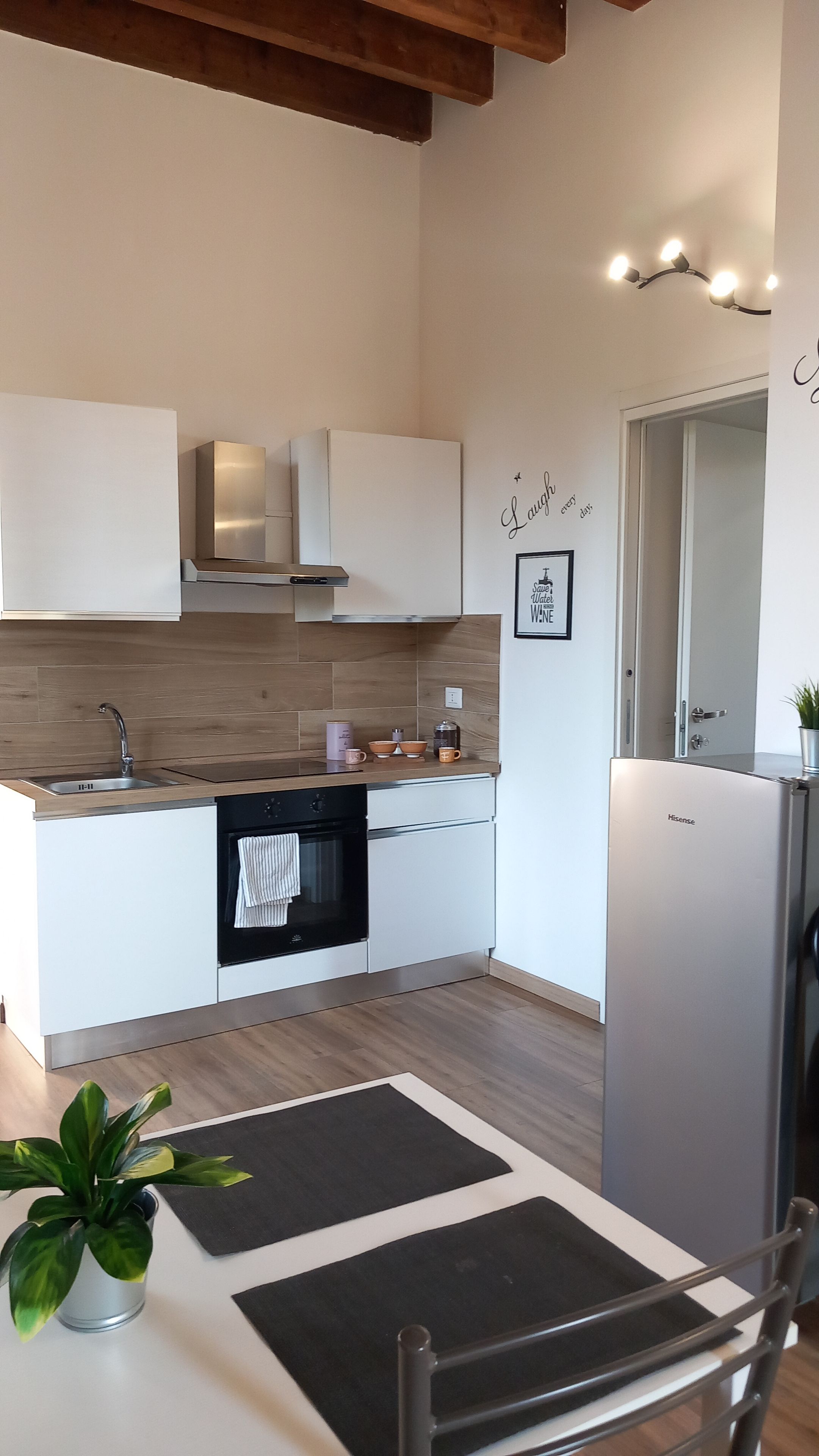 Una cucina moderna con mobili bianchi, frigorifero in acciaio inossidabile e soffitto in legno.