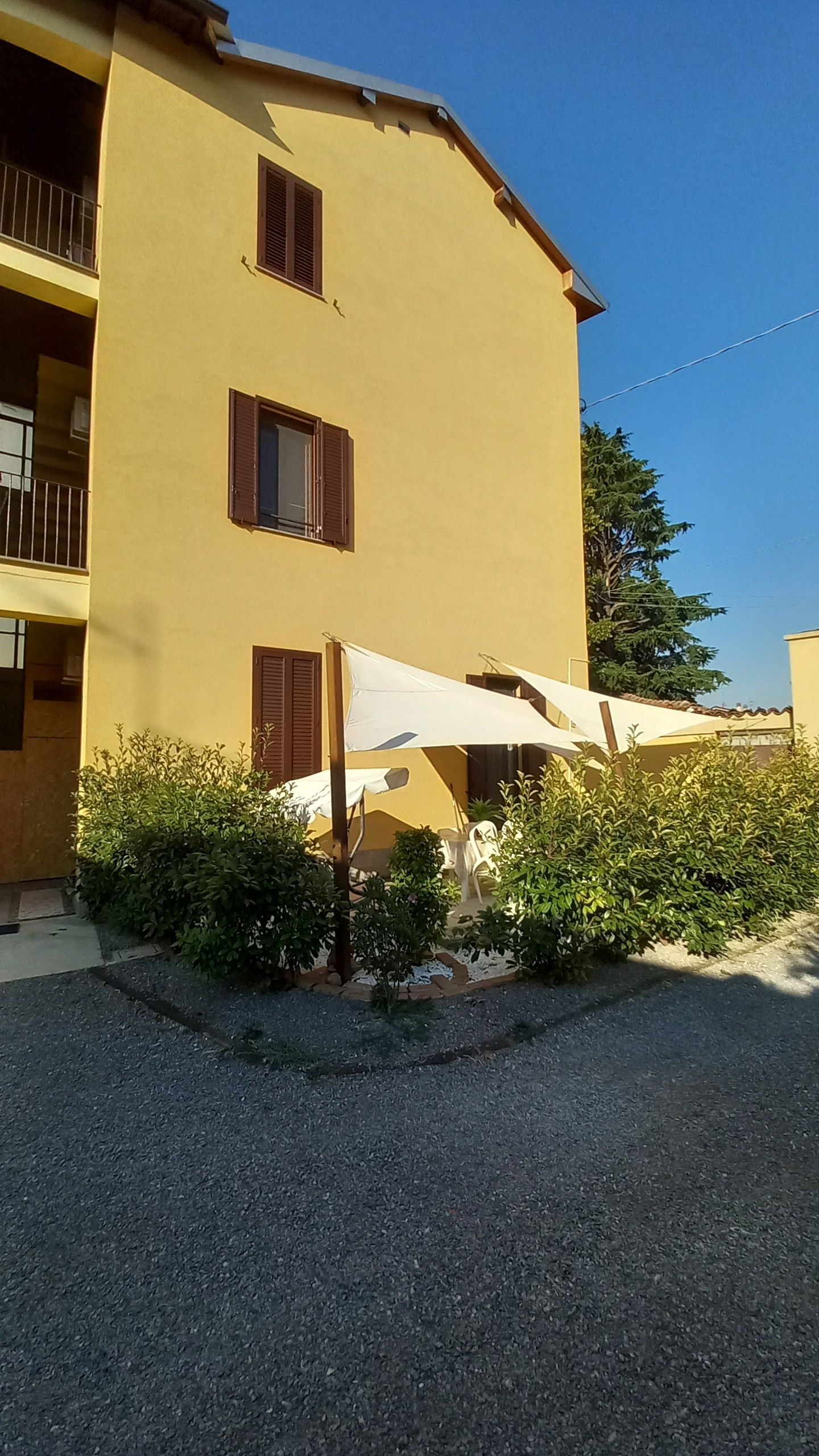 Ein zweistöckiges Gebäude mit gelber Fassade, einem Balkon und einer überdachten Außenbereich mit Sonnenschirmen.