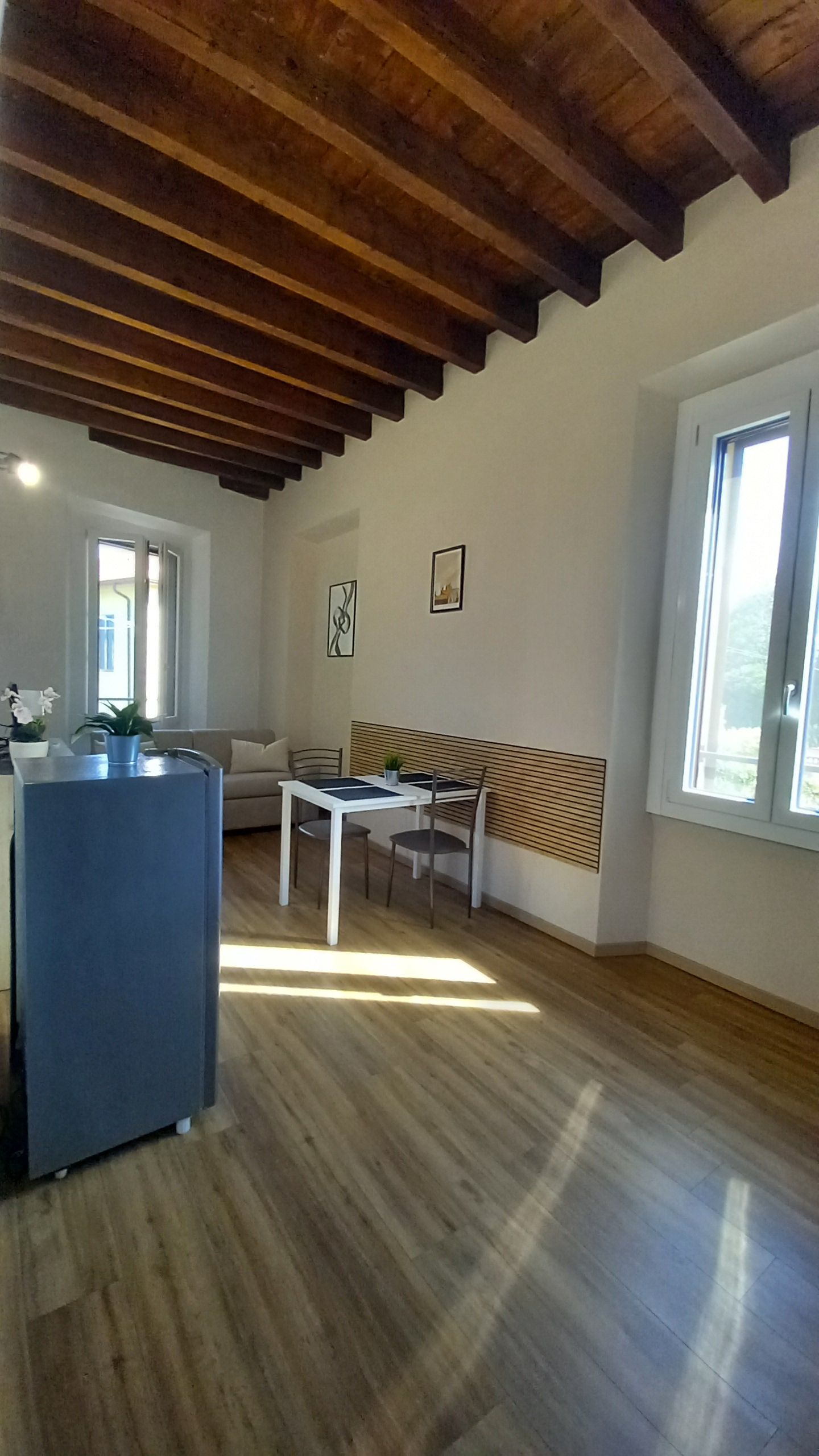 A spacious room with a wooden ceiling, a sofa, a dining table, and a large window.