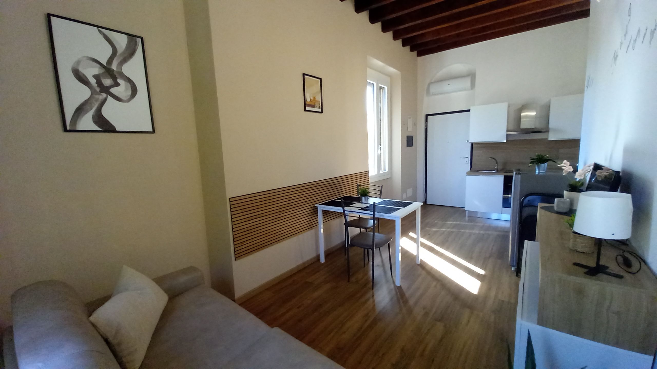 Ein modernes Wohnzimmer mit Sofa, Esstisch mit Stühlen, Küchenzeile mit Spüle und Schränken sowie einem Flur, der in ein weiteres Zimmer führt.